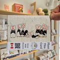 Card with penguins holding signs saying 'I Love You' held by a hand in a store setting.