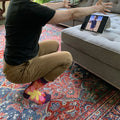 A pair of women's crew socks with a dark purple background and a vibrant, large floral pattern in shades of red, fuchsia, pink, and yellow. Text on one sock reads "Watch out. I'll fuckin' hug you."