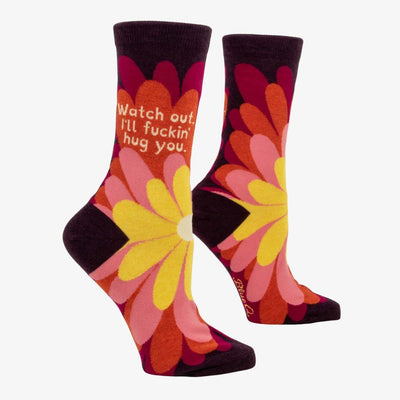 A pair of women's crew socks with a dark purple background and a vibrant, large floral pattern in shades of red, fuchsia, pink, and yellow. Text on one sock reads 