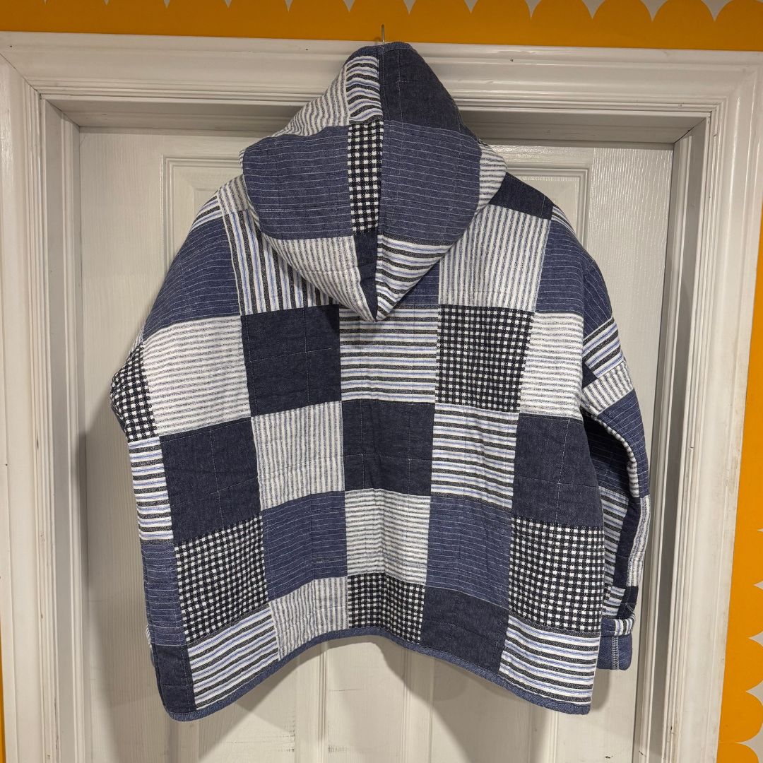 A hooded patchwork jacket made from navy, blue, and white striped and checkered fabrics, hanging on a white paneled door.