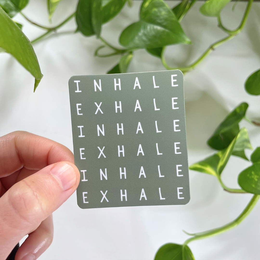 Card with 'INHALE EXHALE' text held by a hand with green leaves in the background