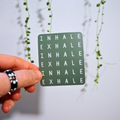 Hand holding a green card with 'INHALE EXHALE' text against a light background with plants.