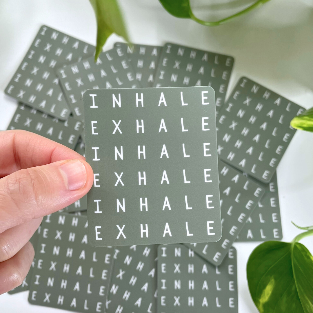 Card with 'INHALE EXHALE' text held by a hand, surrounded by more cards on a light background.