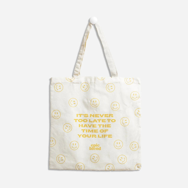 A white tote bag with a yellow smiley face design. The text 