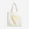 A white tote bag with a yellow smiley face design. The text around the smiley face reads: 