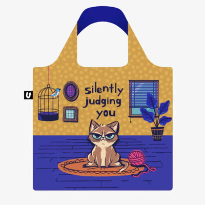 A blue and yellow tote bag with a humorous illustration of a grumpy cat sitting on a rug and silently judging the viewer. The text 