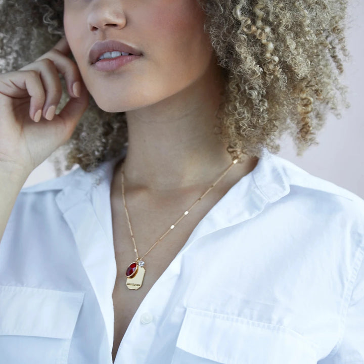A gold necklace with a red garnet stone pendant. The pendant also has the word 