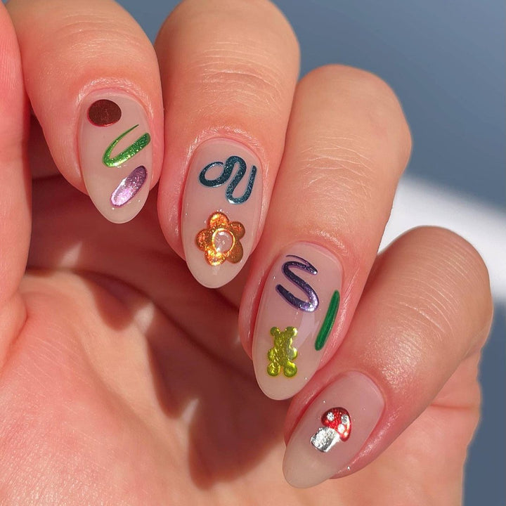 A sheet of colorful nail art stickers with various shapes like rainbows, mushrooms, flowers, and hearts. The sheet is purple and has the brand name 