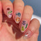 A sheet of colorful nail art stickers with various shapes like rainbows, mushrooms, flowers, and hearts. The sheet is purple and has the brand name 