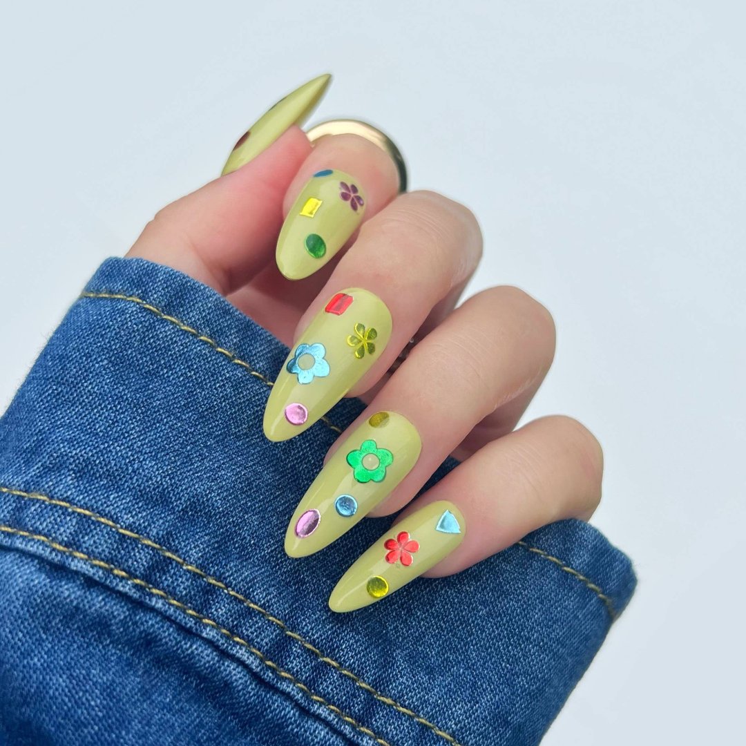 A sheet of colorful nail art stickers with various shapes like rainbows, mushrooms, flowers, and hearts. The sheet is purple and has the brand name "Deco Beauty" printed on it. There's a section titled "JELLY" and instructions on how to apply the stickers.