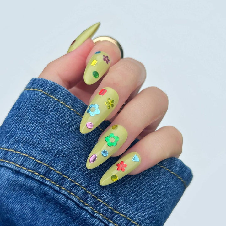 A sheet of colorful nail art stickers with various shapes like rainbows, mushrooms, flowers, and hearts. The sheet is purple and has the brand name 