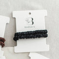Black hair scrunchies on a Barbays branded card against a gray background