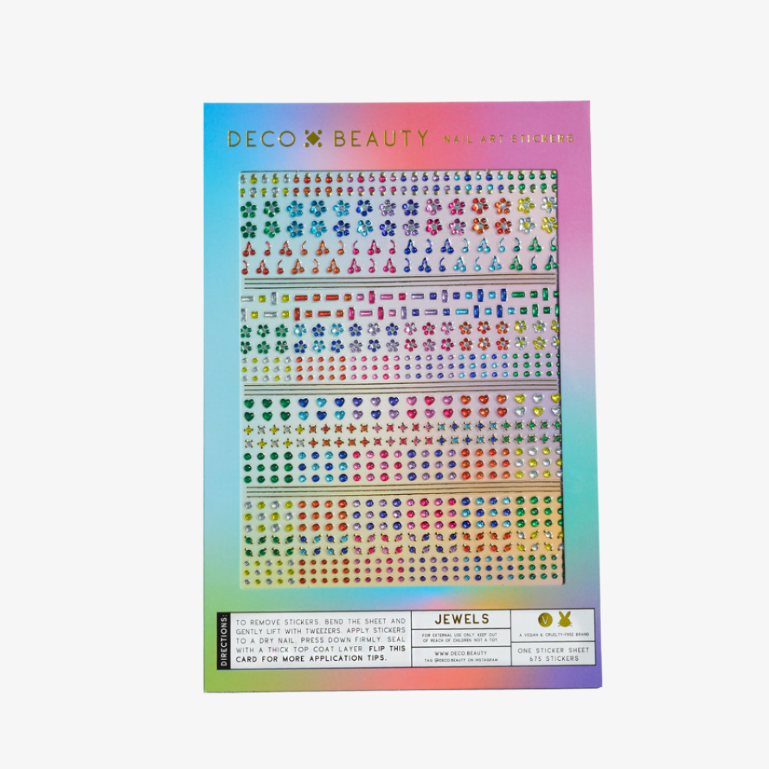 A sheet of colorful nail art stickers with various shapes like stars, hearts, flowers, and geometric designs. The sheet is holographic and has the brand name "Deco Beauty" printed on it. There's a section titled "JEWELS" and instructions on how to apply the stickers.