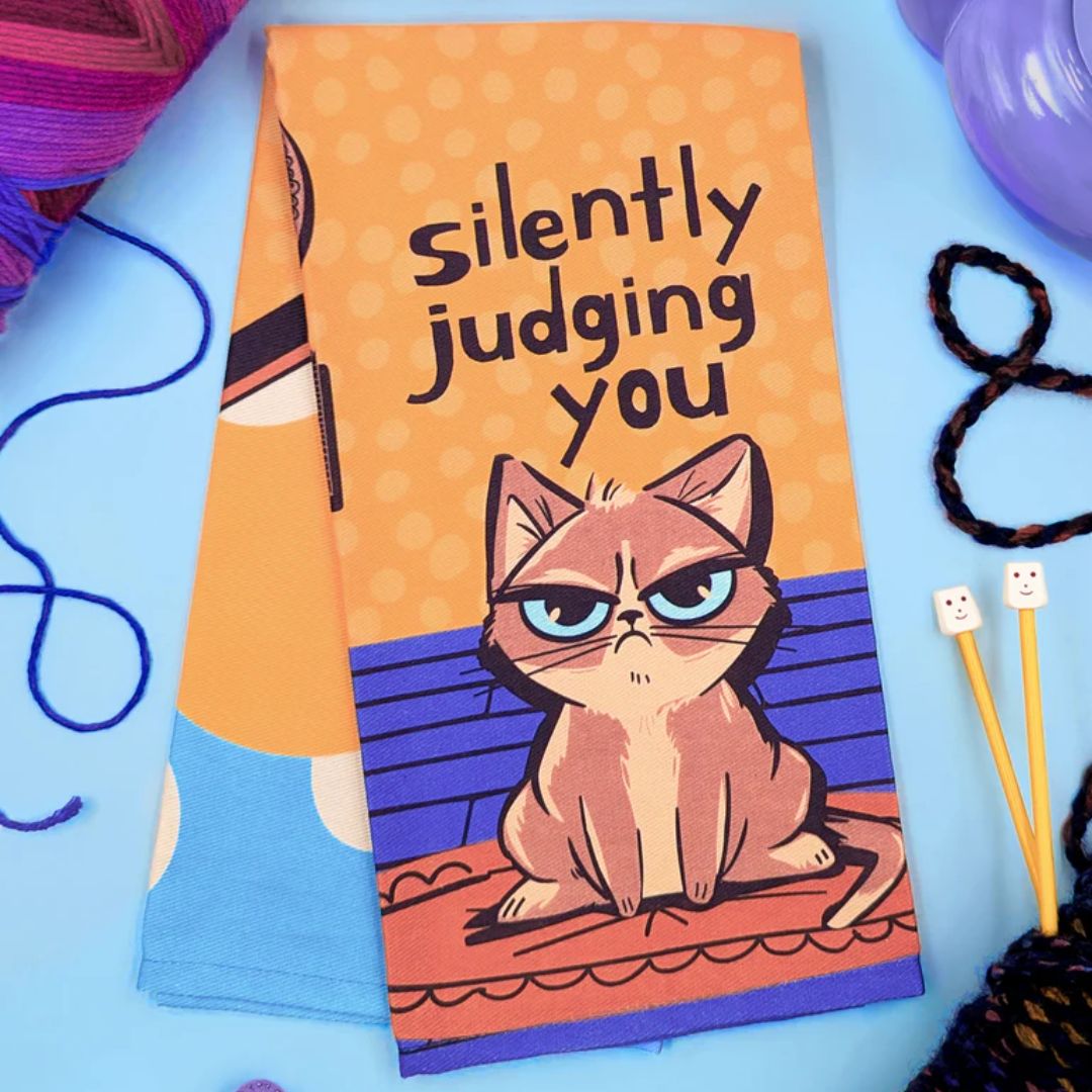 Towel with a cat illustration and text 'silently judging you' on an orange background.