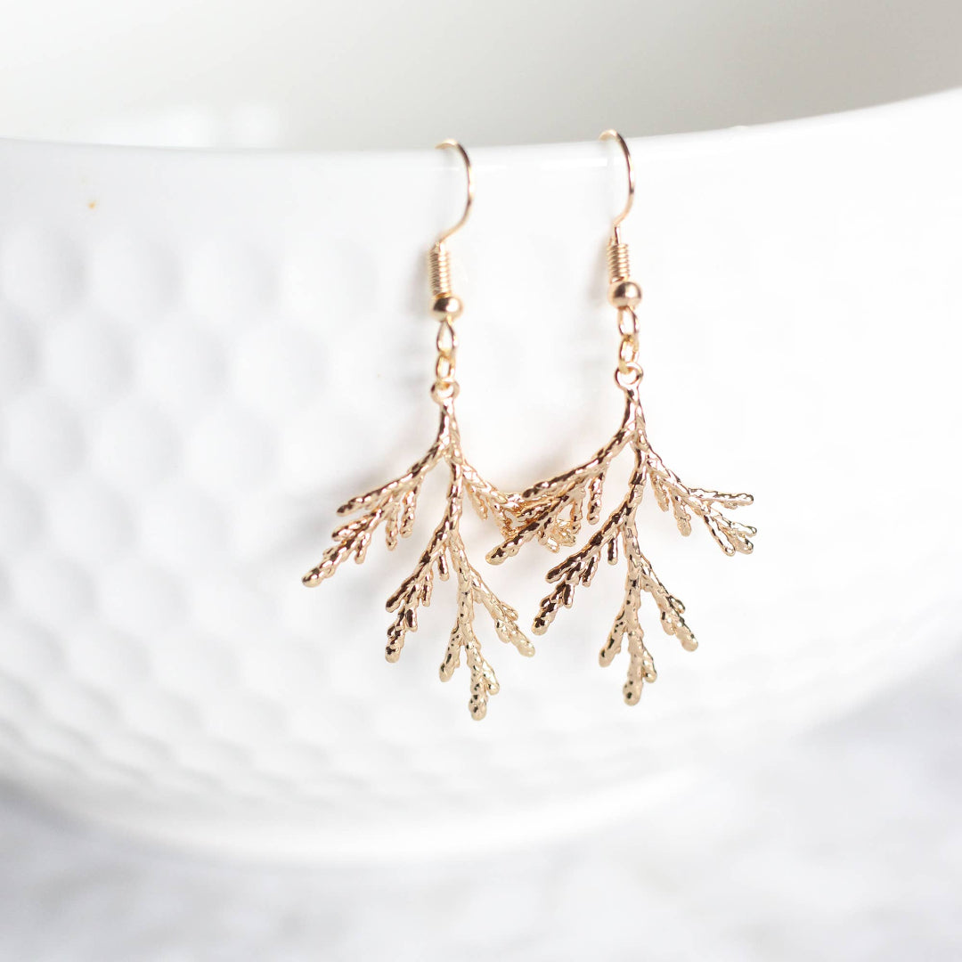 Gold branch-like earrings on a white surface