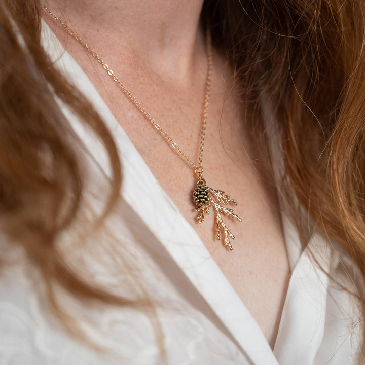 a gold-colored pine cone and branch pendant with a delicate chain.