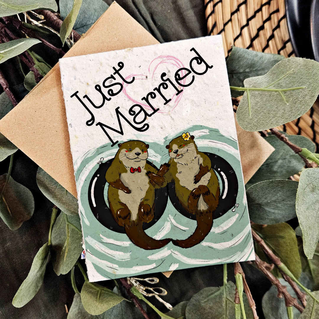 Card with 'Just Married' text and otter illustration, surrounded by greenery