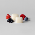 Four white cylindrical cookies with red, blue, and black berries on a light gray background