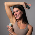 Woman using an underarm deodorant stick on a gray background