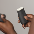 Person holding a black deodorant stick with a white cap against a neutral background