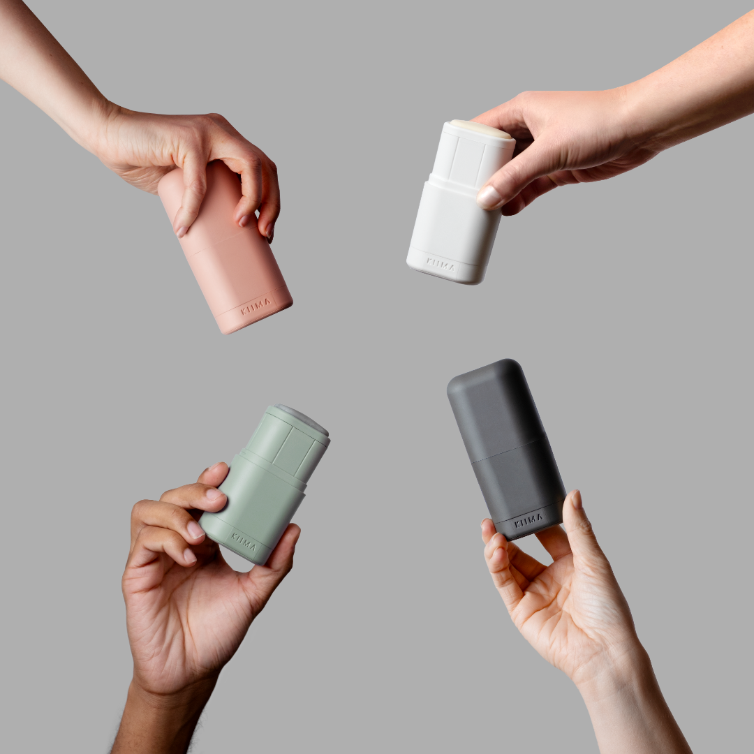 Four hands holding cylindrical containers in pink, white, green, and gray against a gray background