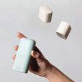 Hand holding a mint green container with marshmallows levitating above it against a light gray background