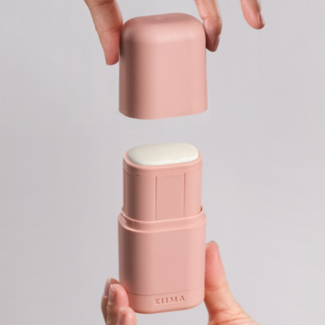 Pink lip balm container with white cap held by hands against a gray background