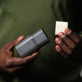 Person holding a gray cylindrical device and a white square block against a dark background