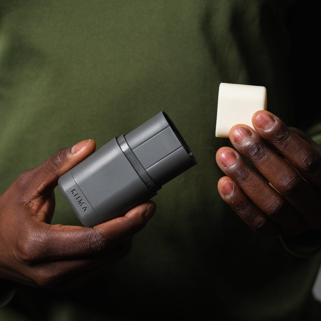 Person holding a gray cylindrical device and a white square block against a dark background
