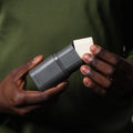 Person holding a gray electronic device with a white component against a dark background