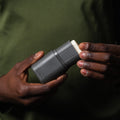 Person holding a gray device with a white component against a dark background