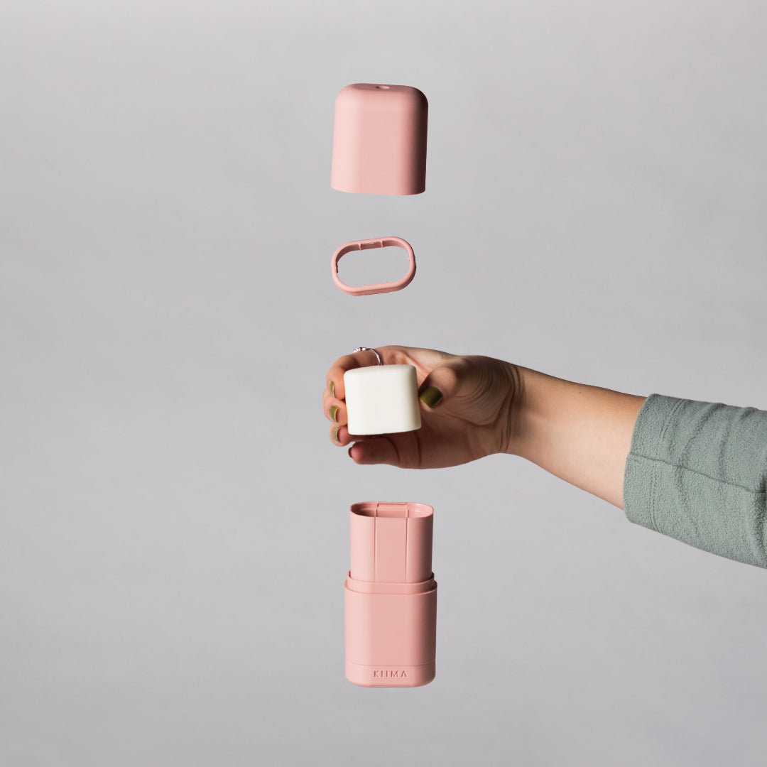 Person holding a pink container with a white lid against a gray background