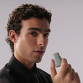 Man holding a small gray object against a plain background