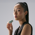 Woman holding a small green object against a plain background