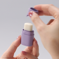 Person holding a small purple container with a white cap against a plain background
