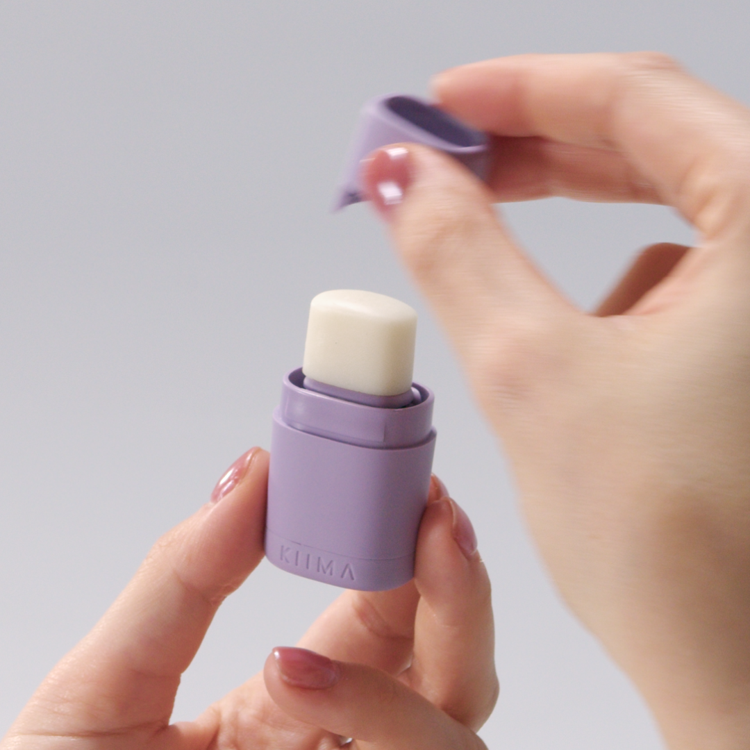 Person holding a small purple container with a white cap against a plain background