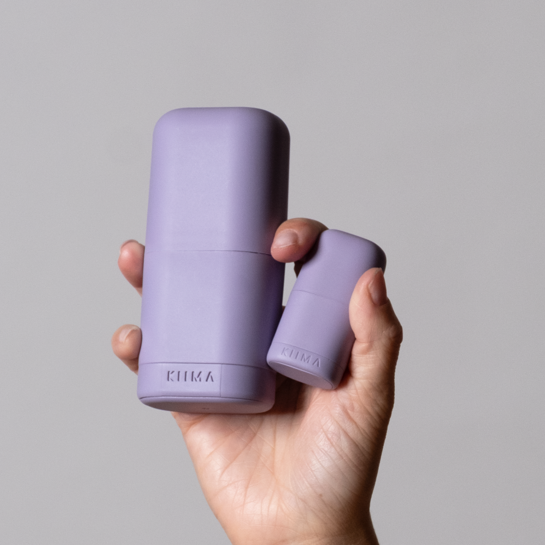 Hand holding two purple cylindrical containers with a brand logo on a gray background
