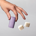 Hand holding a purple Klima container with two white caps on a gray background