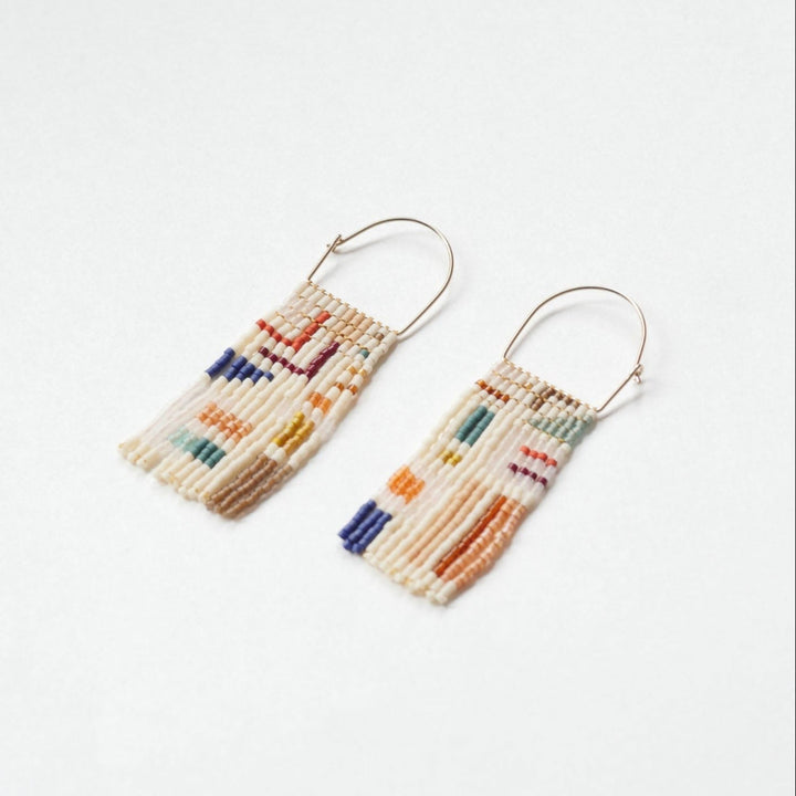 A pair of rectangular, tapestry-style earrings hand-stitched with small Japanese glass beads in an abstract, painterly pattern featuring shades of cream, red, burgundy, orange, yellow, teal, and blue. They hang from delicate, half-circle 14 KT gold filled wire hoops.