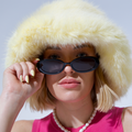 Person wearing a fluffy yellow hat and sunglasses with a plain background