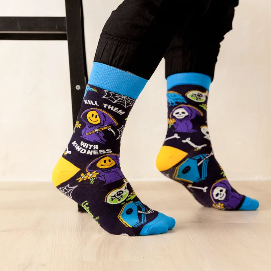 A person wearing black pants and bright blue crew socks with a spooky cartoon print, sitting on a black stool in a studio setting.