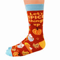 A pair of red socks with a fall-themed design. The socks feature pumpkins, cinnamon sticks, whipped cream, and the phrase "LET'S SPICE THINGS UP."