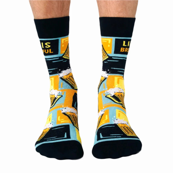 A pair of crew socks featuring a beer mug design. The socks are mostly black with yellow and blue accents. The text 