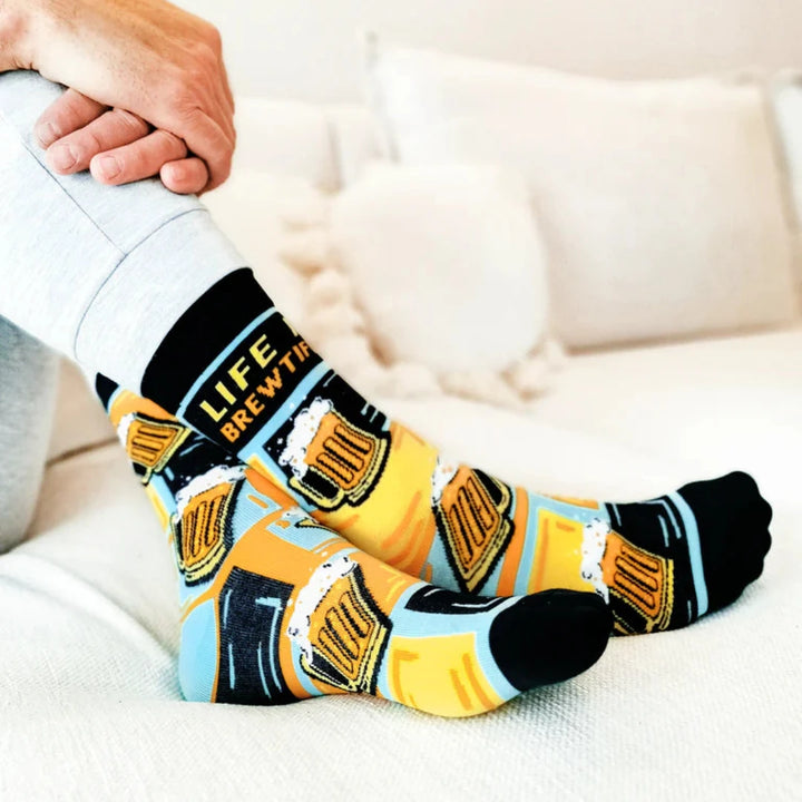 A pair of crew socks featuring a beer mug design. The socks are mostly black with yellow and blue accents. The text 