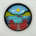 A Paint By Layers Craft Kit featuring a circular shadow box with a pre-designed landscape scene. The scene depicts a lake at sunset, with a person in a canoe and trees on the shore. The kit includes layers of wood, paint, and instructions. The title of the kit is "Lake Life Shadow Box."