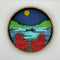 A Paint By Layers Craft Kit featuring a circular shadow box with a pre-designed landscape scene. The scene depicts a lake at sunset, with a person in a canoe and trees on the shore. The kit includes layers of wood, paint, and instructions. The title of the kit is 