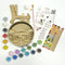 A Paint By Layers Craft Kit featuring a circular shadow box with a pre-designed landscape scene. The scene depicts a lake at sunset, with a person in a canoe and trees on the shore. The kit includes layers of wood, paint, and instructions. The title of the kit is 