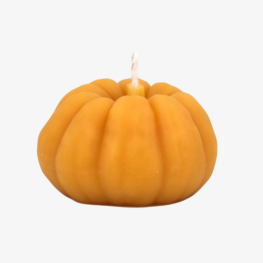 A small, pumpkin-shaped beeswax candle. The candle is orange with detailed ridges and a wick in the center.