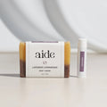 Bar of lavender lemongrass soap and a stick of lavender lip balm on a light surface with a neutral background.