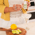 Person pouring a drink into a martini glass with a lemon and lime on a cutting board.